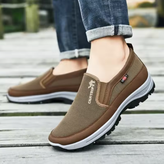Brun ortopedisk slip-on sko för herr buren utomhus på trädäck, visar passform på foten