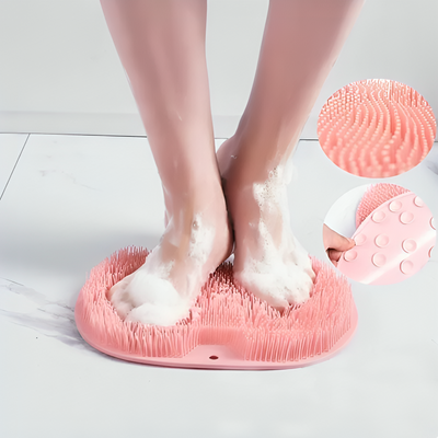 Fötter som tvättas på rosa skrubbmatta med soapskum, närbild visar mattans silikonborstar och sugproppar på undersidan

