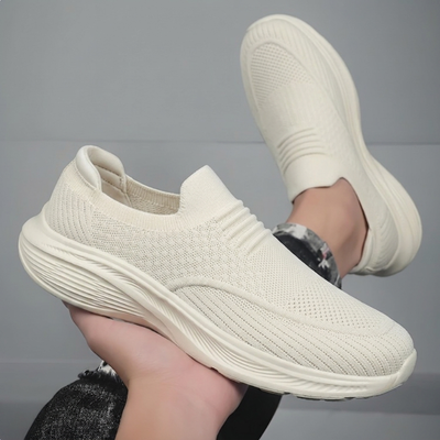 Beige slip-on komfortsko hållen i handen, visar tjock stötdämpande sula underifrån
