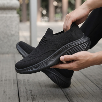 Händer som enkelt tar på svart slip-on komfortsko utan snörning utomhus på trädäck