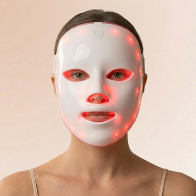Kvinna med InfraRelief™ LED-ansiktsmask i vitt med rött ljus, framifrån mot beige bakgrund