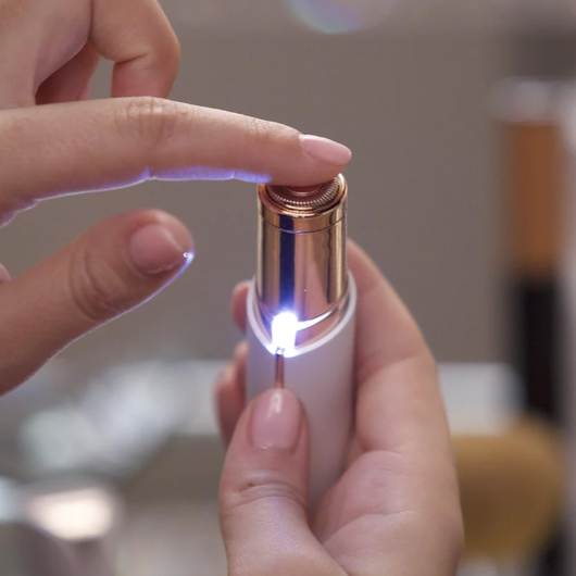 Närbild på ansiktstrimmer med roterande rakhuvud och LED-belysning – finger trycker på knappen för att aktivera