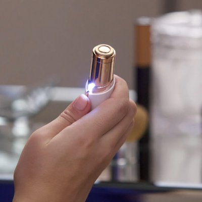 Kompakt ansiktstrimmer för hårborttagning i vitt och roséguld med LED-belysning – hålls i hand mot badrumsbakgrund