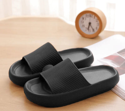 Svarta ergonomiska tofflor med tjock stöddämpande sula på träbord hemma – bekväma tofflor för vardag och återhämtning